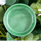 Open jar of mint green metallic paint against a background of foliage.