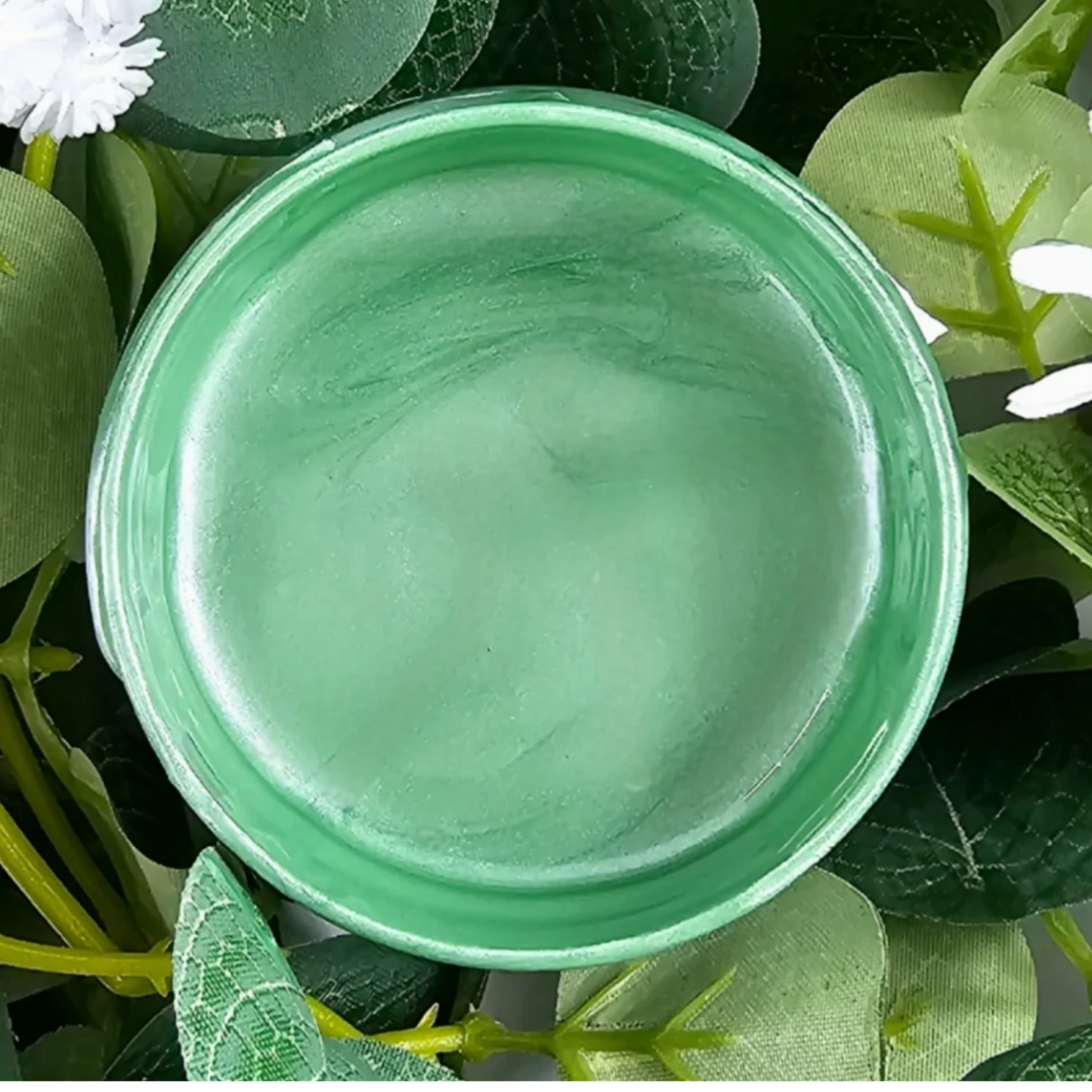 Open jar of mint green metallic paint against a background of foliage.