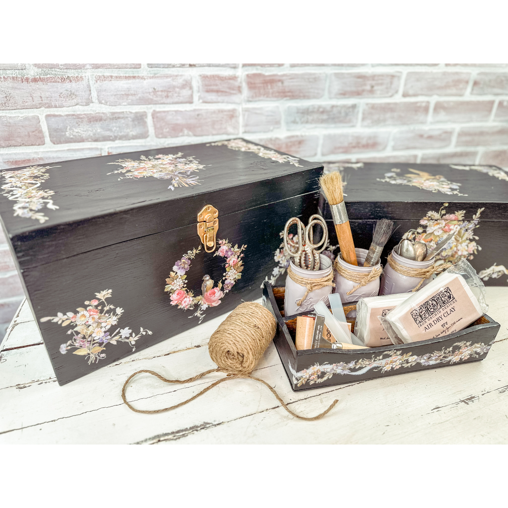 Decorative black box with floral designs containing stationery items on a wooden surface.
