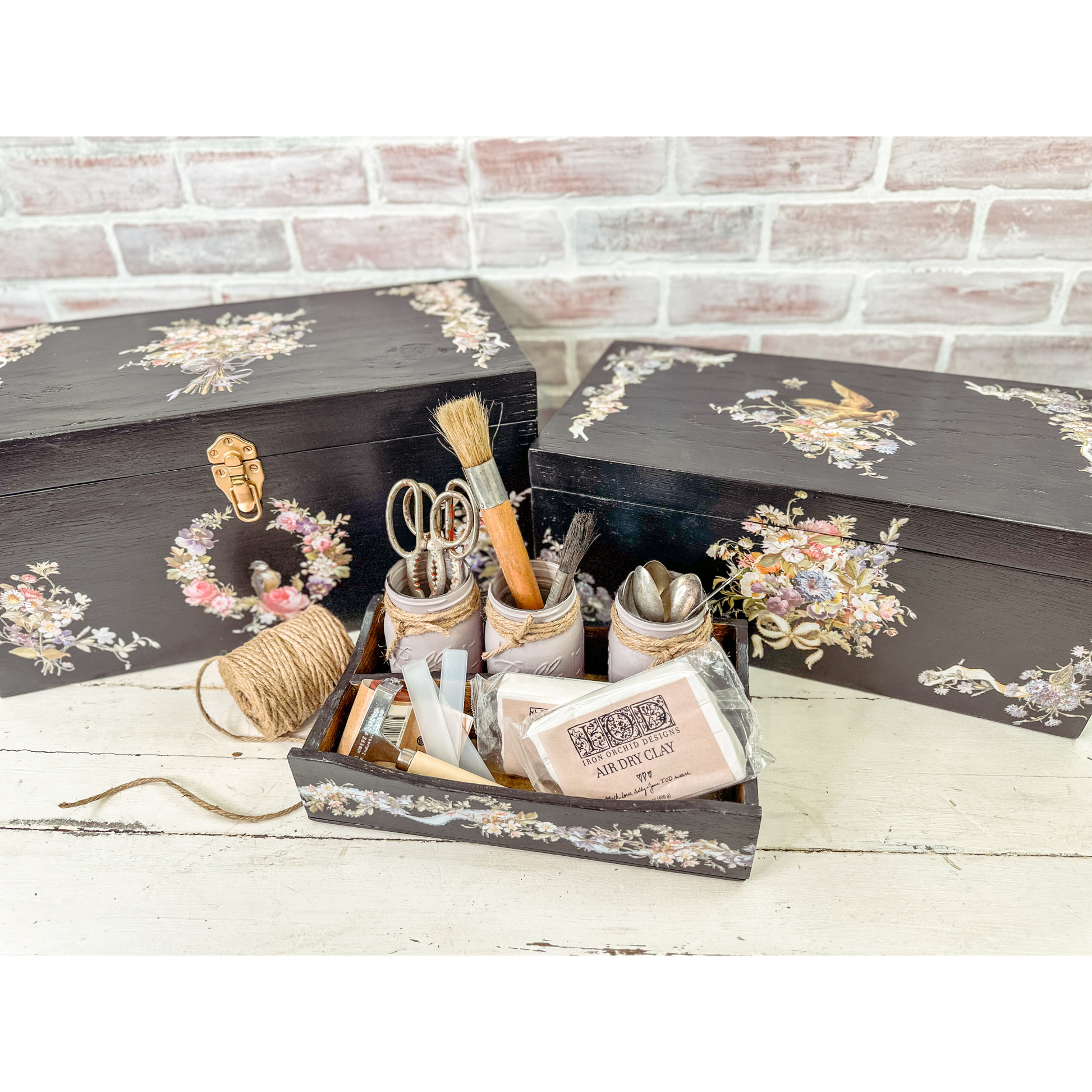 Decorative black box with floral patterns containing stationery items on a white wooden surface.