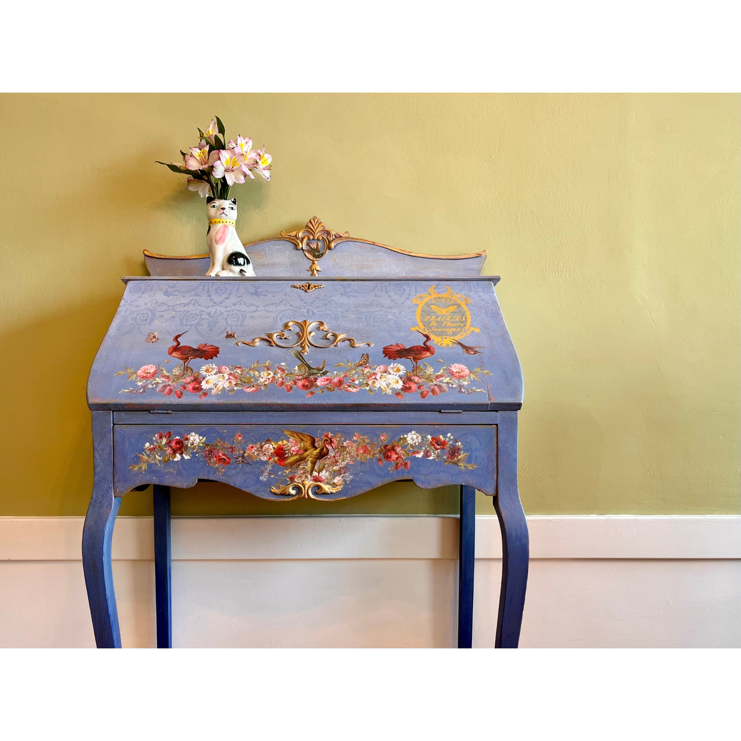 Decorative blue desk with floral and gold designs against a yellow wall.