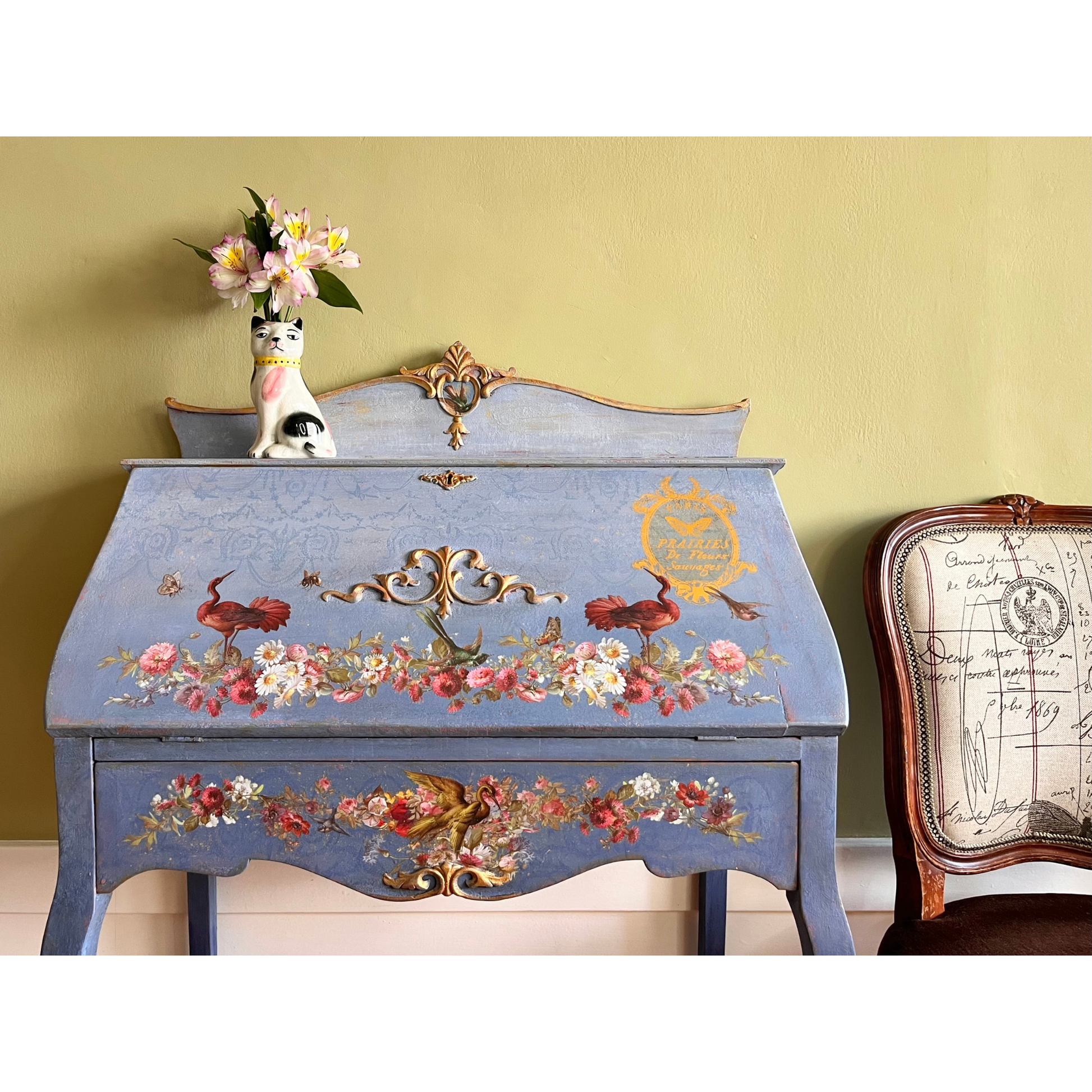 Decorative desk with floral and bird designs against a yellow wall.
