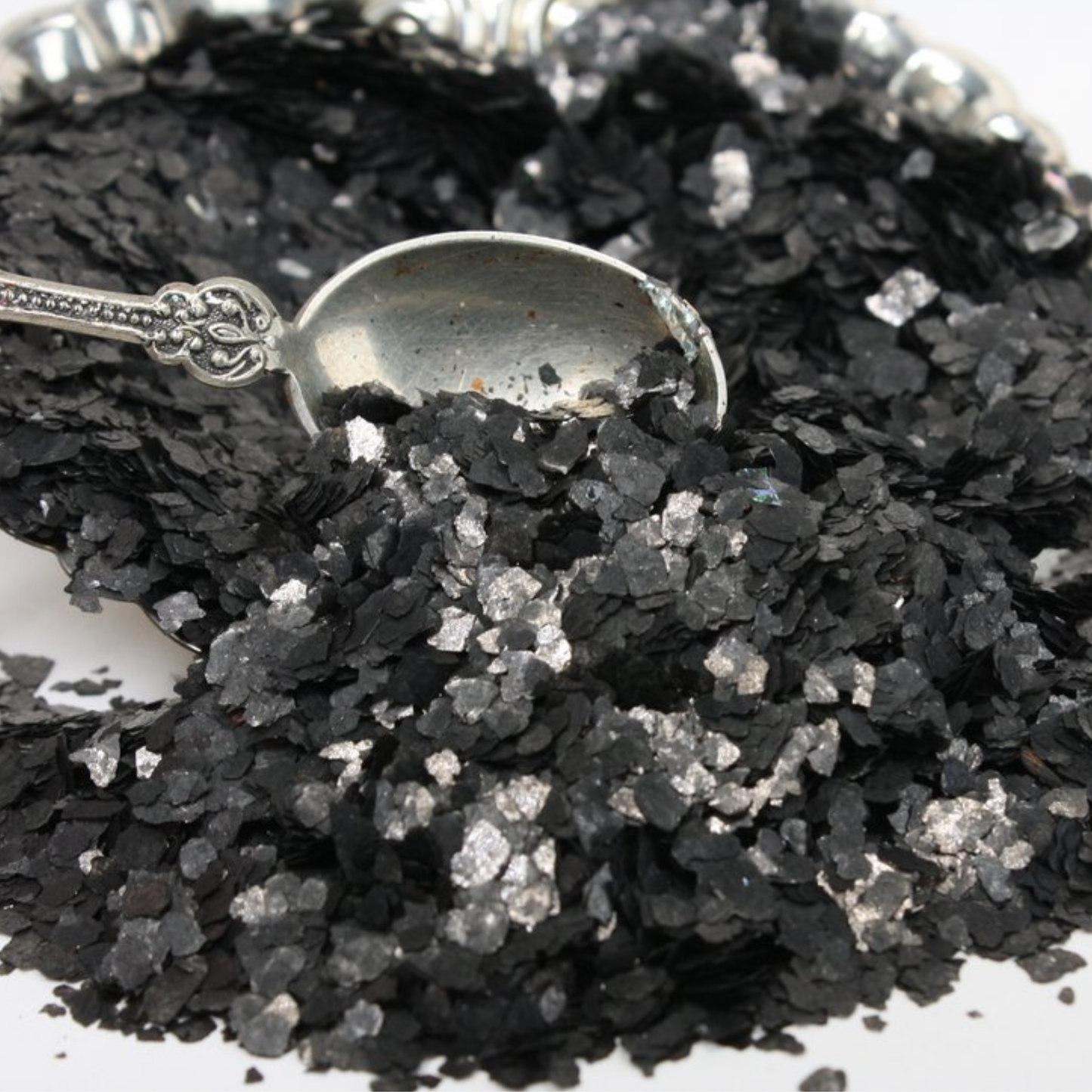Black flakes with a silver spoon for scale on a white background