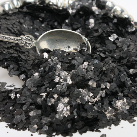 Black flakes with a silver spoon for scale on a white background