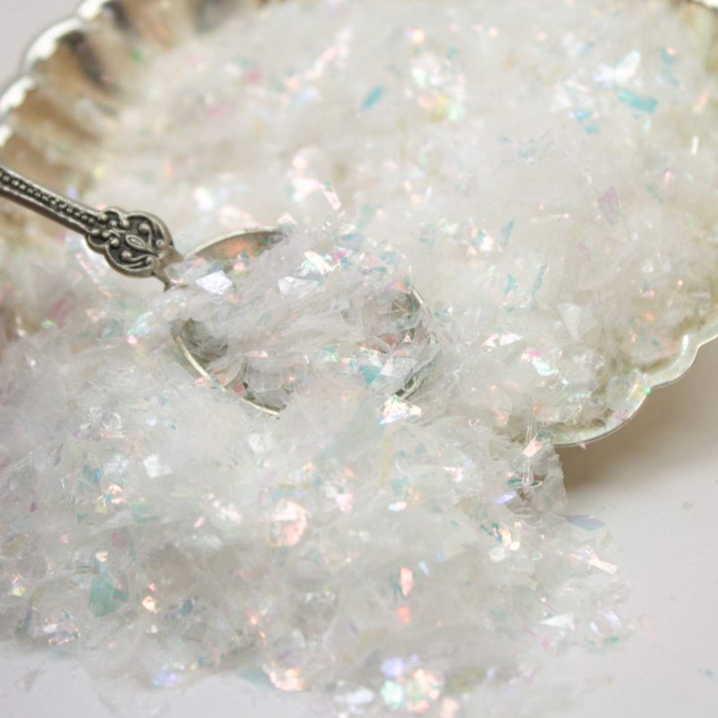 Sparkling white glitter with a silver spoon on a white background
