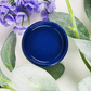 Image of open jar of deep blue paint with blue flowers and leaves on a white background.