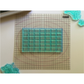 A translucent aqua blue rectangular grid stamp block placed on a gridded Mini Thin Mount, with decortive stamps partially visible around the edges.