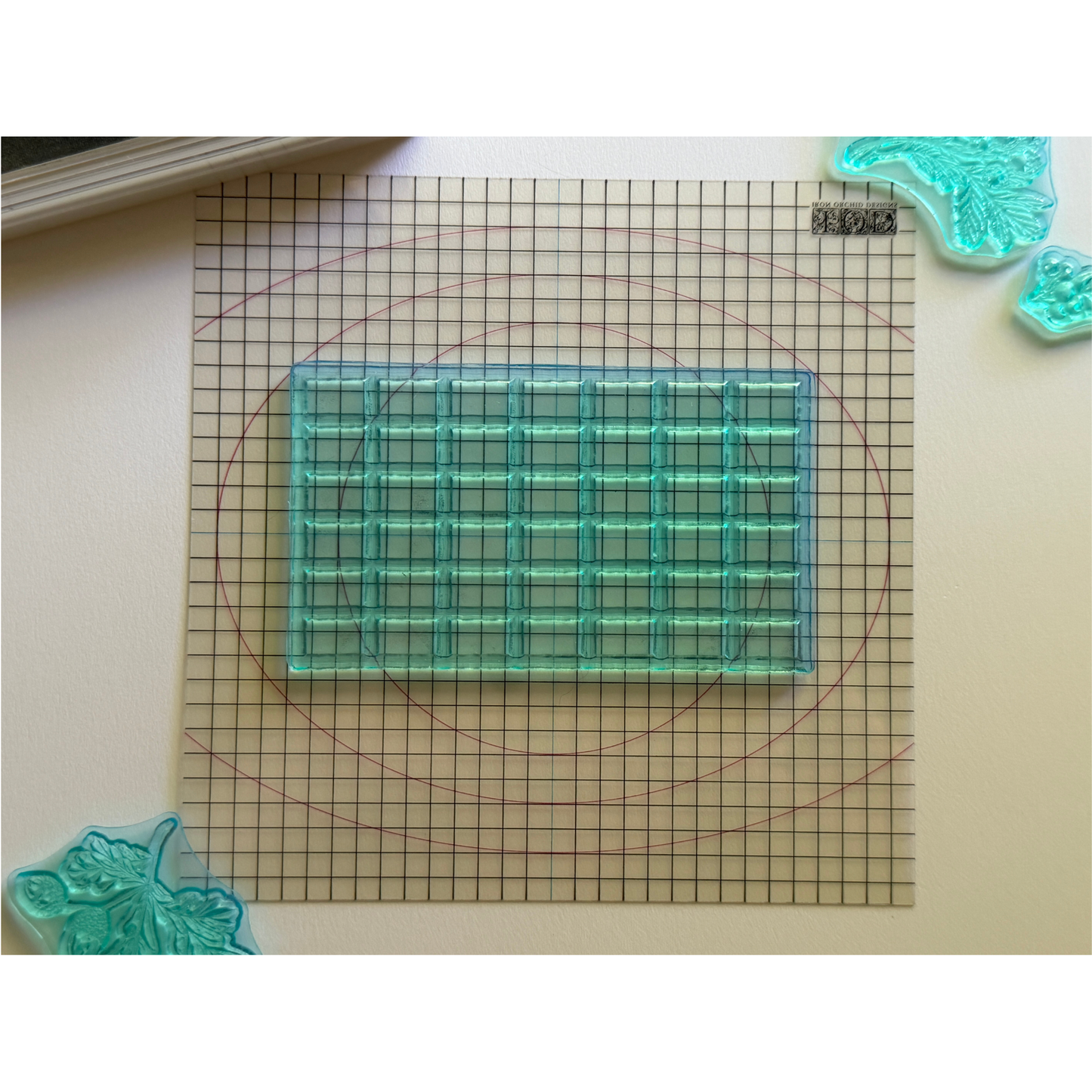A translucent aqua blue rectangular grid stamp block placed on a gridded Mini Thin Mount, with decortive stamps partially visible around the edges.