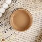 Image of open jar of golden beige colored paint on sepia toned cursive text ephemera.