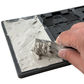 A close-up of a hand using a metal ruler to  level clay-like material into a silicone mold.