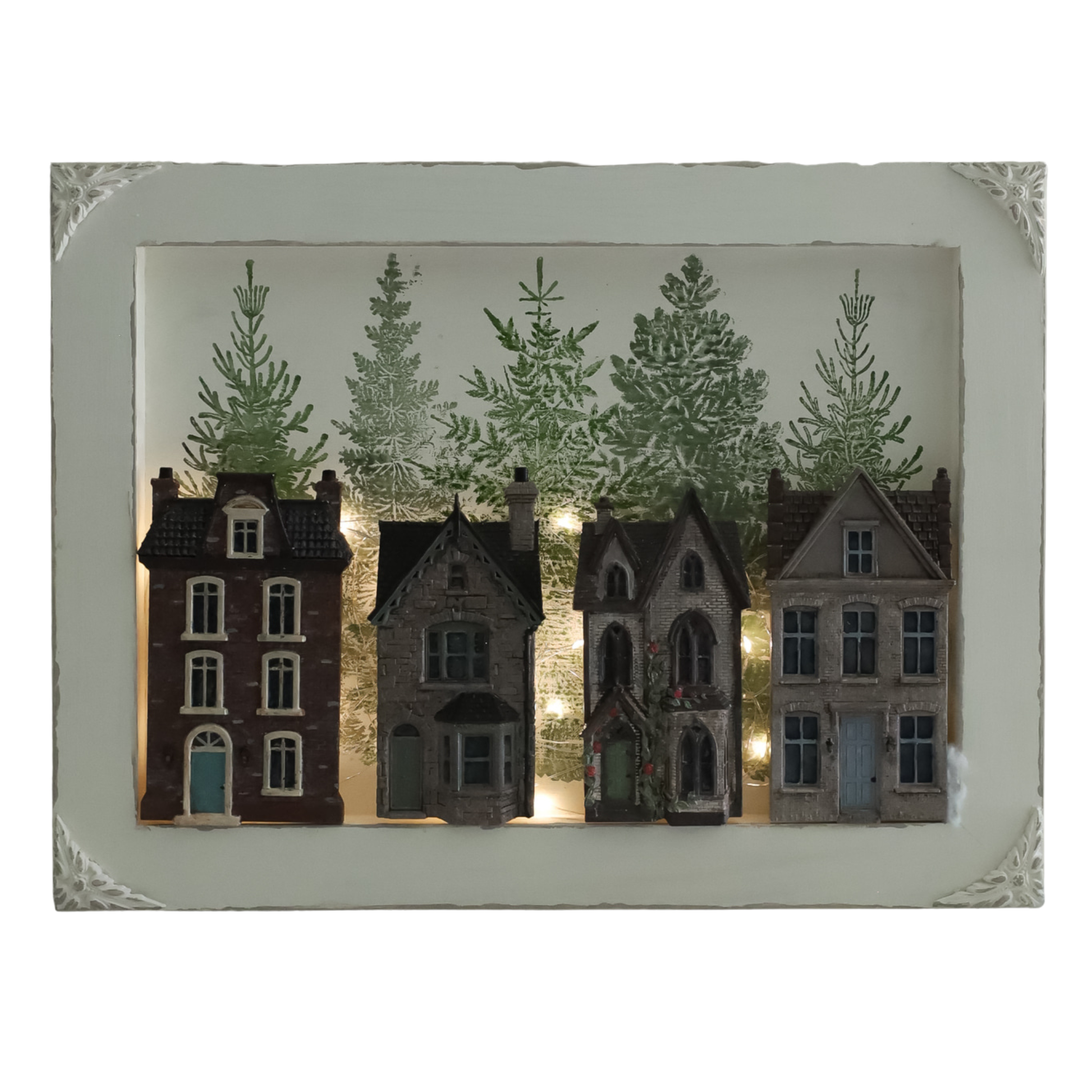 A decorative framed wall hanging featuring four miniature house silhouettes in front of a printed winter forest backdrop with warm string lights, set in an off-white frame.