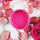 Image of an open jar of bubblegum pink paint with pink rose petals and pearls.