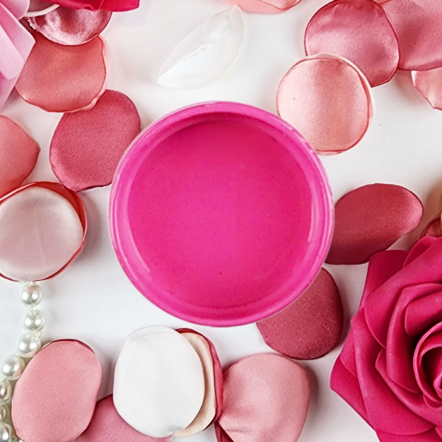 Image of an open jar of bubblegum pink paint with pink rose petals and pearls.