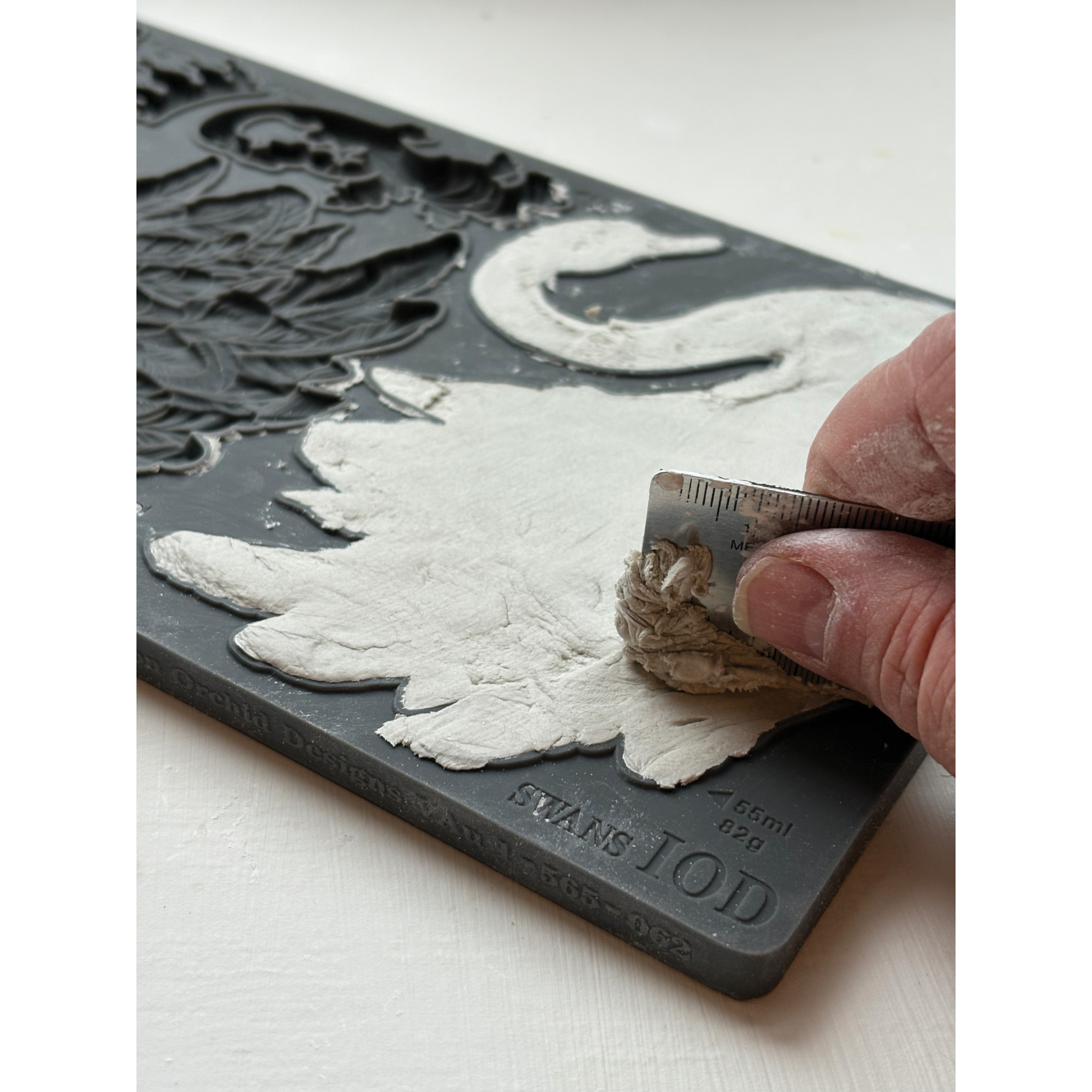 Hand using a tool to add clay into IOD Swans Mould by Iron Orchid Designs.