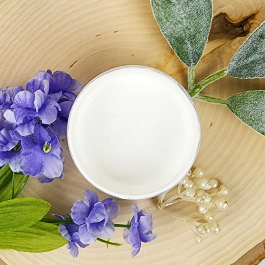 Image of open jar of bright white paint with blue flowers and leaves on a wood background.