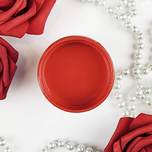 Image of an open jar of bright red paint with red roses and pearls in the background.