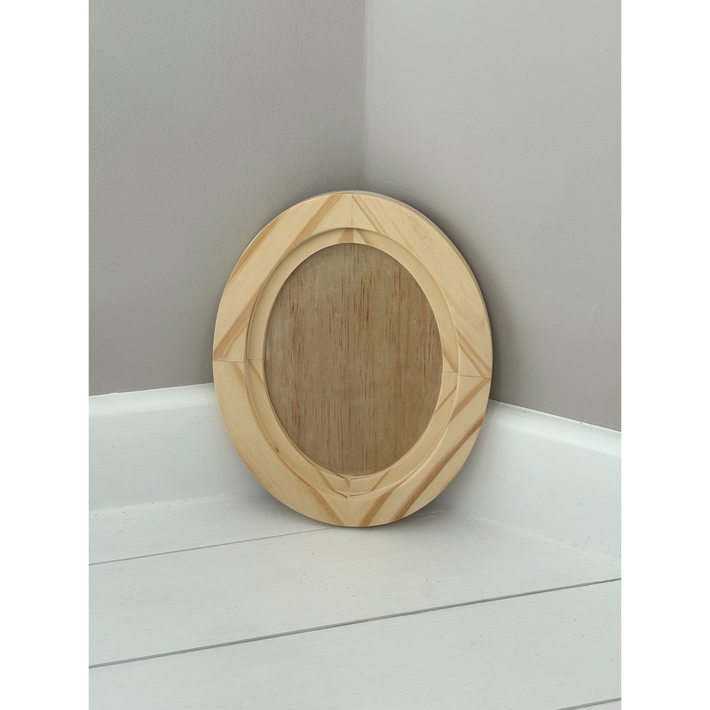 Small wooden oval frame on a white surface with a gray wall background