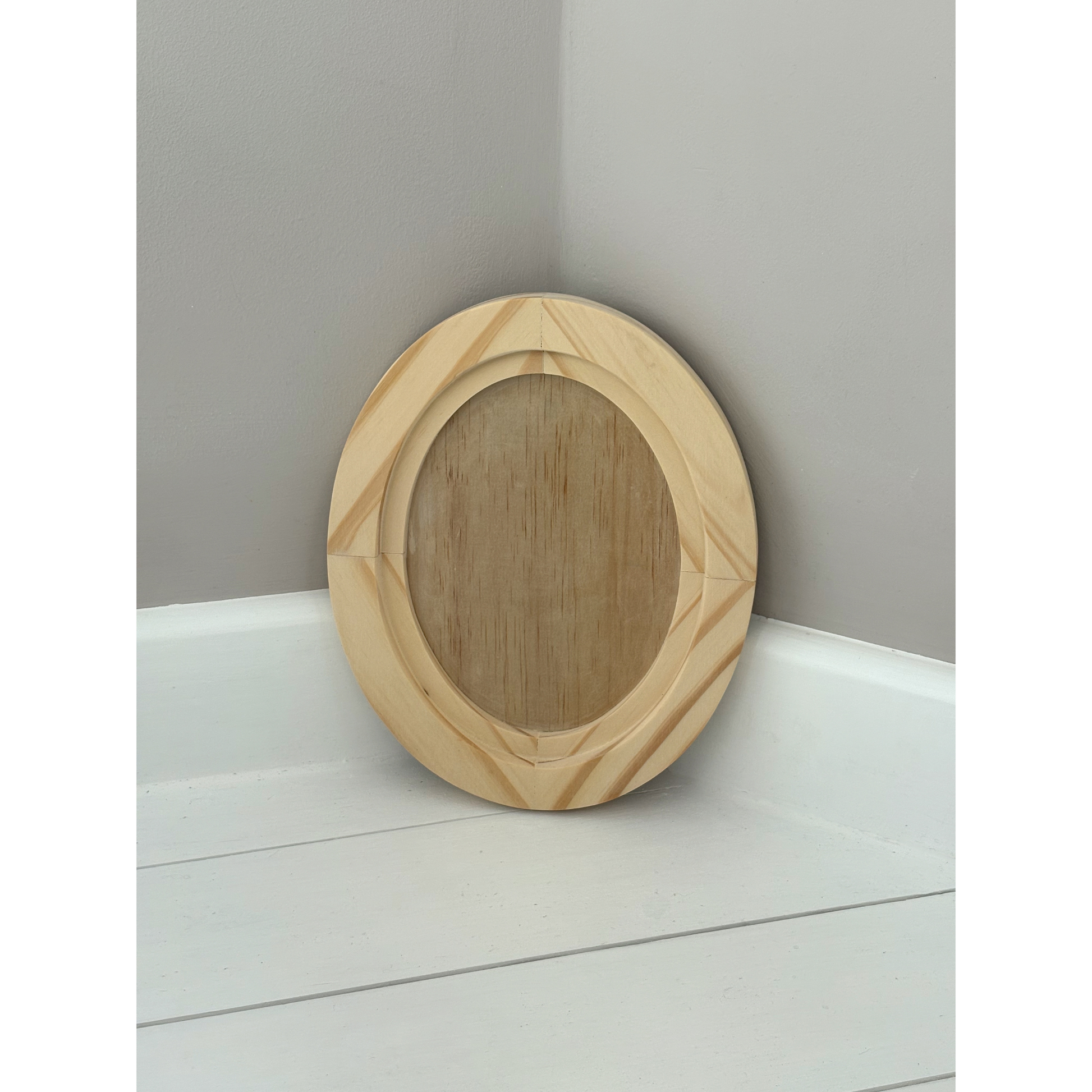 Small wooden oval frame on a white surface with a gray wall background