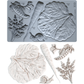 Silicone mold with leaf and vegetable shapes on a gray background with casting examples in white clay.