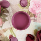 Image of open jar of deep pink paint on a background of printed colorful text and pink rose petals.
