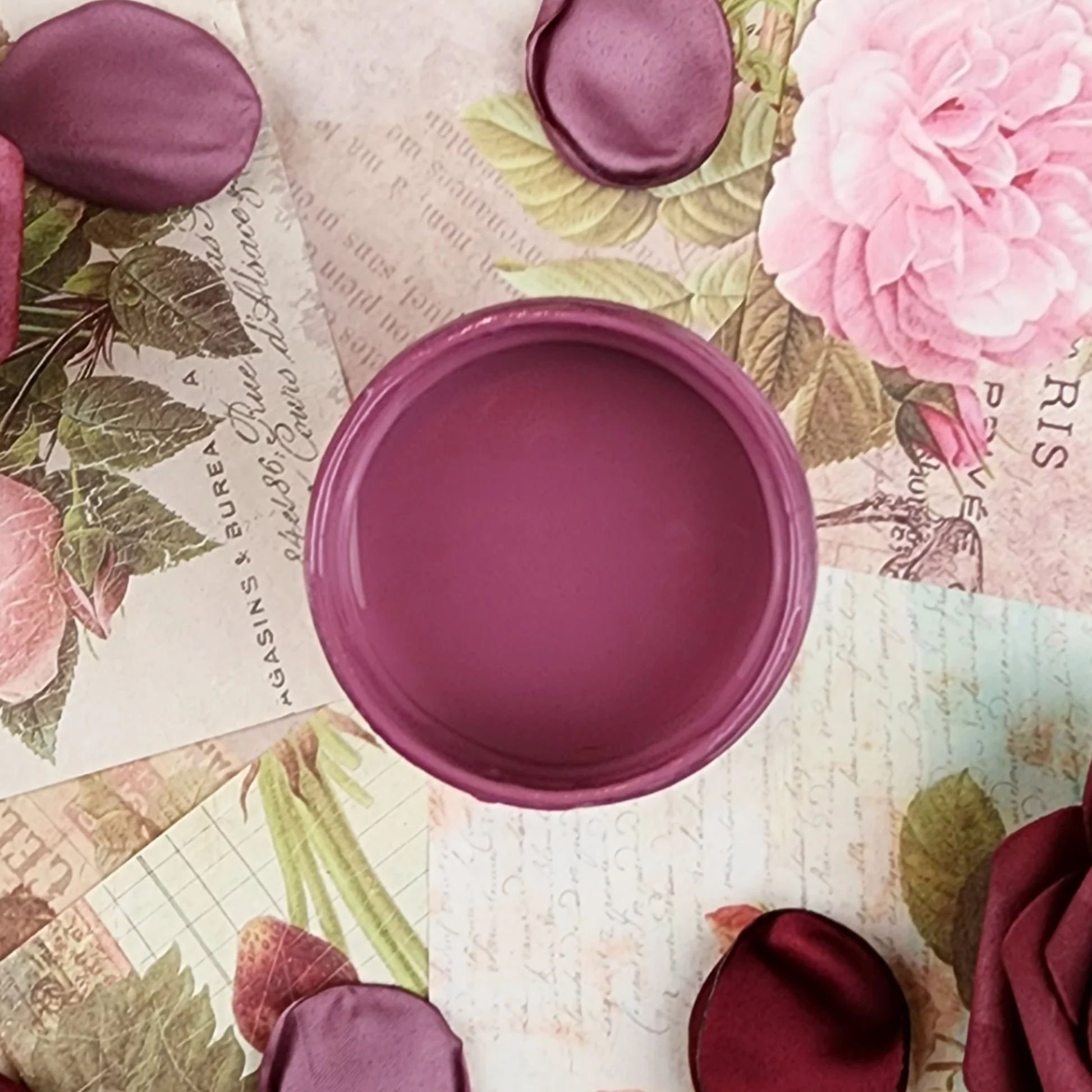 Image of open jar of deep pink paint on a background of printed colorful text and pink rose petals.
