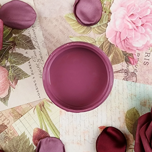 Image of open jar of deep pink paint on a background of printed colorful text and pink rose petals.