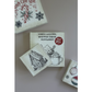 A set of vintage-style Christmas-themed square signs with illustrated designs, including a gingerbread house, candy cane, snowflake, peppermint hot cocoa, and holiday ornaments, arranged on a neutral surface.