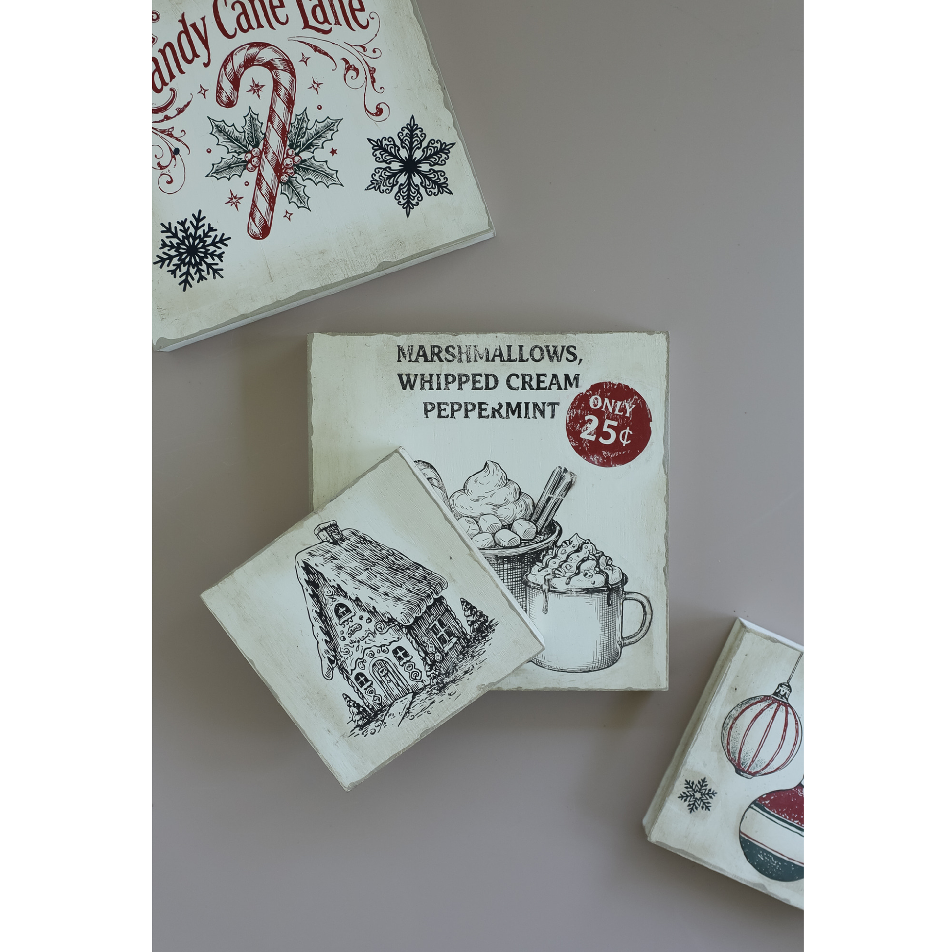 A set of vintage-style Christmas-themed square signs with illustrated designs, including a gingerbread house, candy cane, snowflake, peppermint hot cocoa, and holiday ornaments, arranged on a neutral surface.