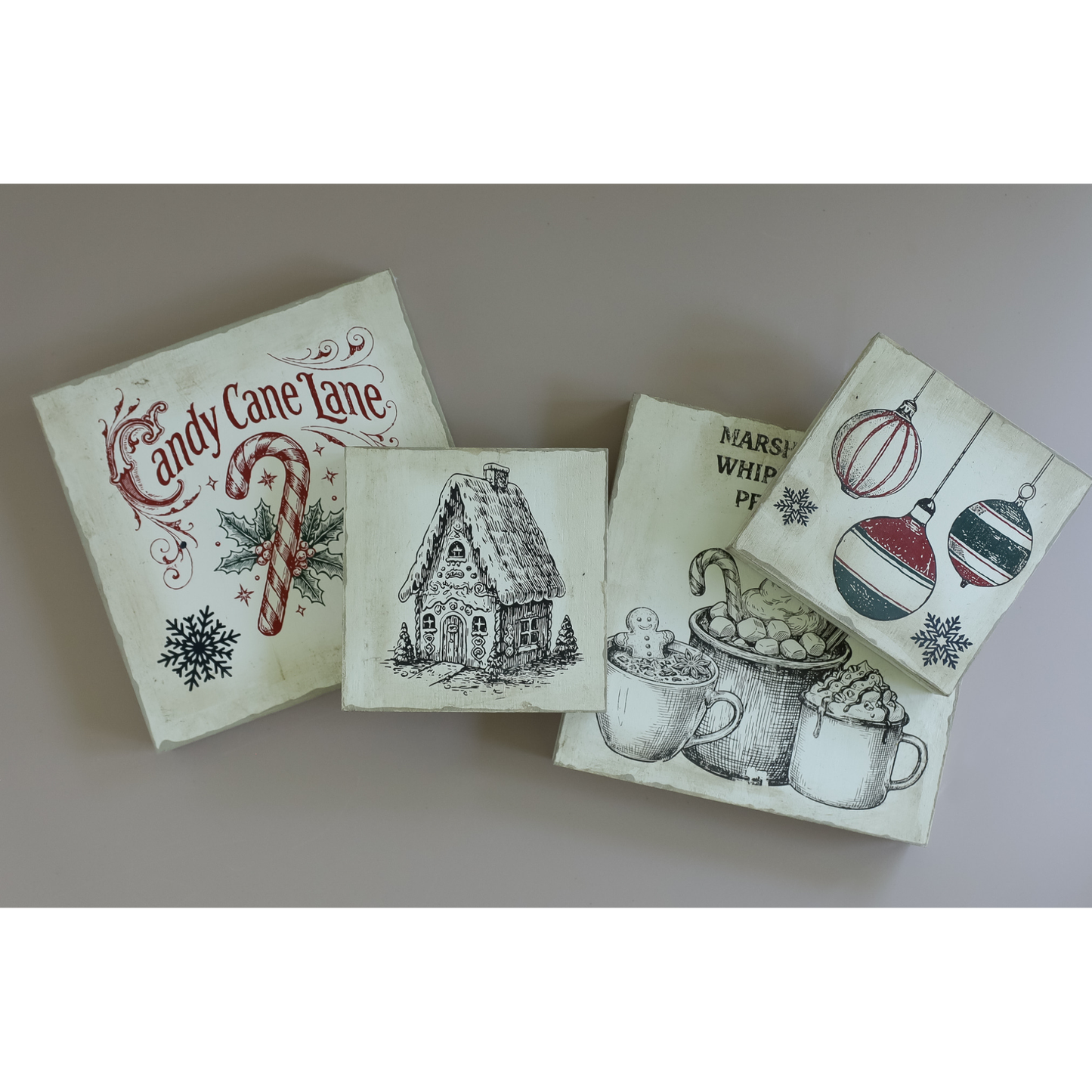 Four square decorative signs or coasters with vintage Christmas illustrations, including a candy cane, gingerbread house, hot cocoa cups, and ornaments, arranged on a neutral gray background.