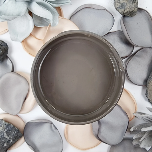 Image of open jar of taupe brown paint on a background of grey and peach flower petals.