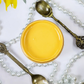 Image of an open jar of canary yellow paint with pears and silver spoons in the background.