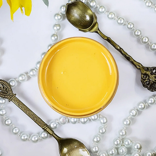 Image of an open jar of canary yellow paint with pears and silver spoons in the background.