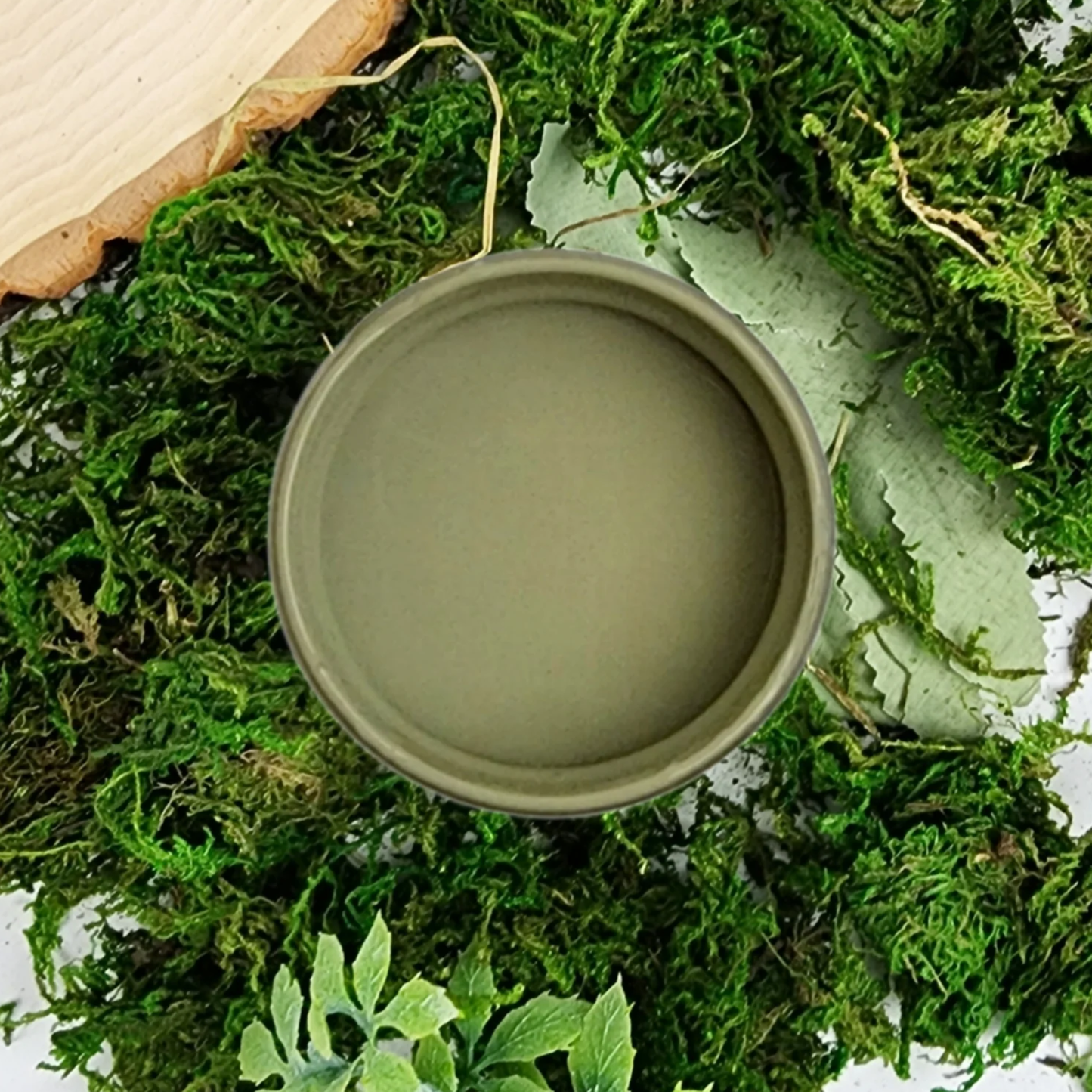 Image of an open jar containing a brownish grey paint on a bed of moss.
