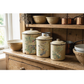 Three vintage-style enamel canisters with lids, decorated with autumn bird and floral IOD transfers, displayed on a rustic wooden kitchen counter alongside matching bowls and copper pots.