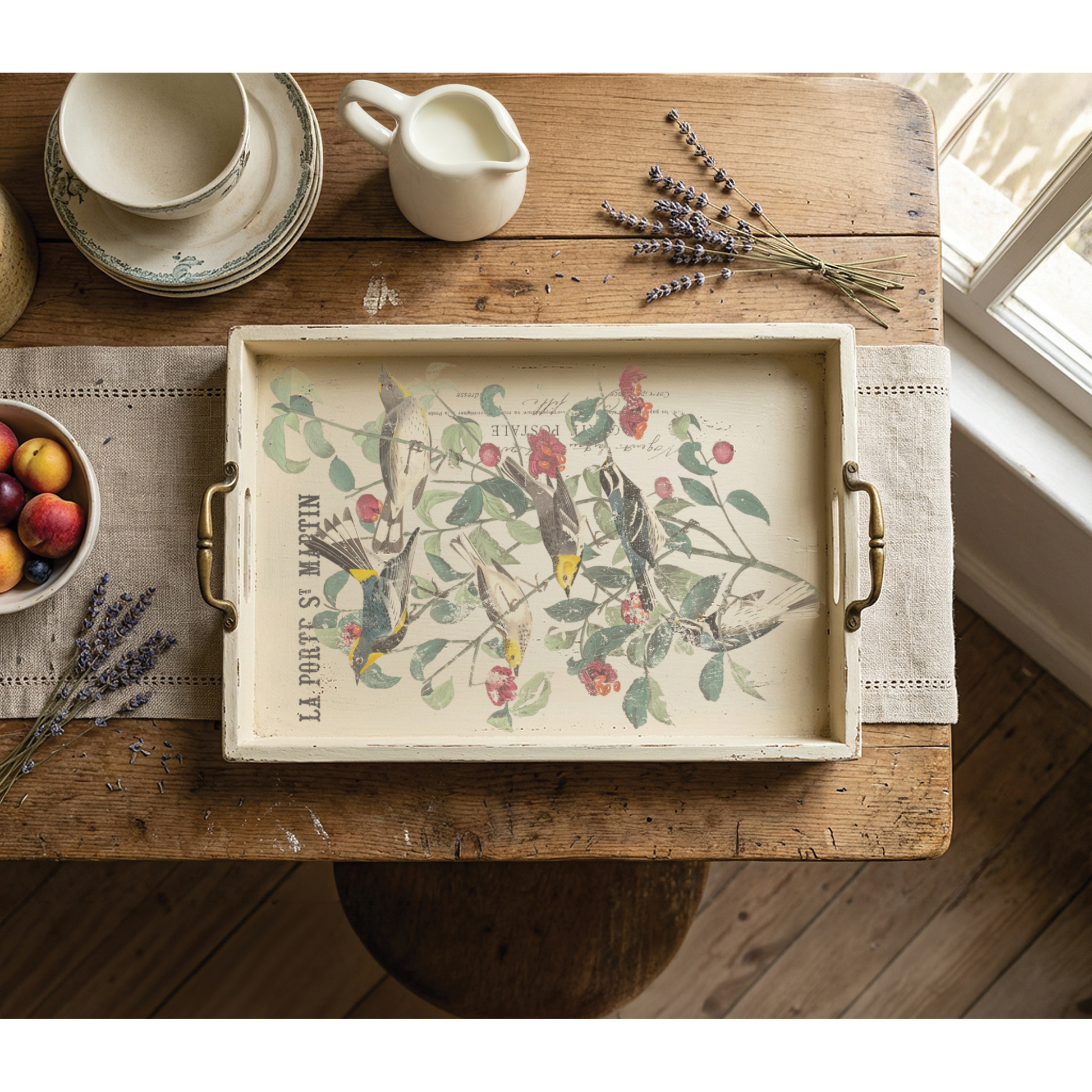 A rectangular decorative serving tray with brass handles sits on a rustic wooden table. The tray has a cream background with a vintage-style botanical IOD Transfer of birds and cherries.