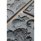 Gray silicone molds with embossed fruit and floral designs, arranged on a light beige surface.