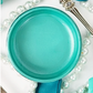 Open jar of turquoise metallic paint with pearls and silverware.