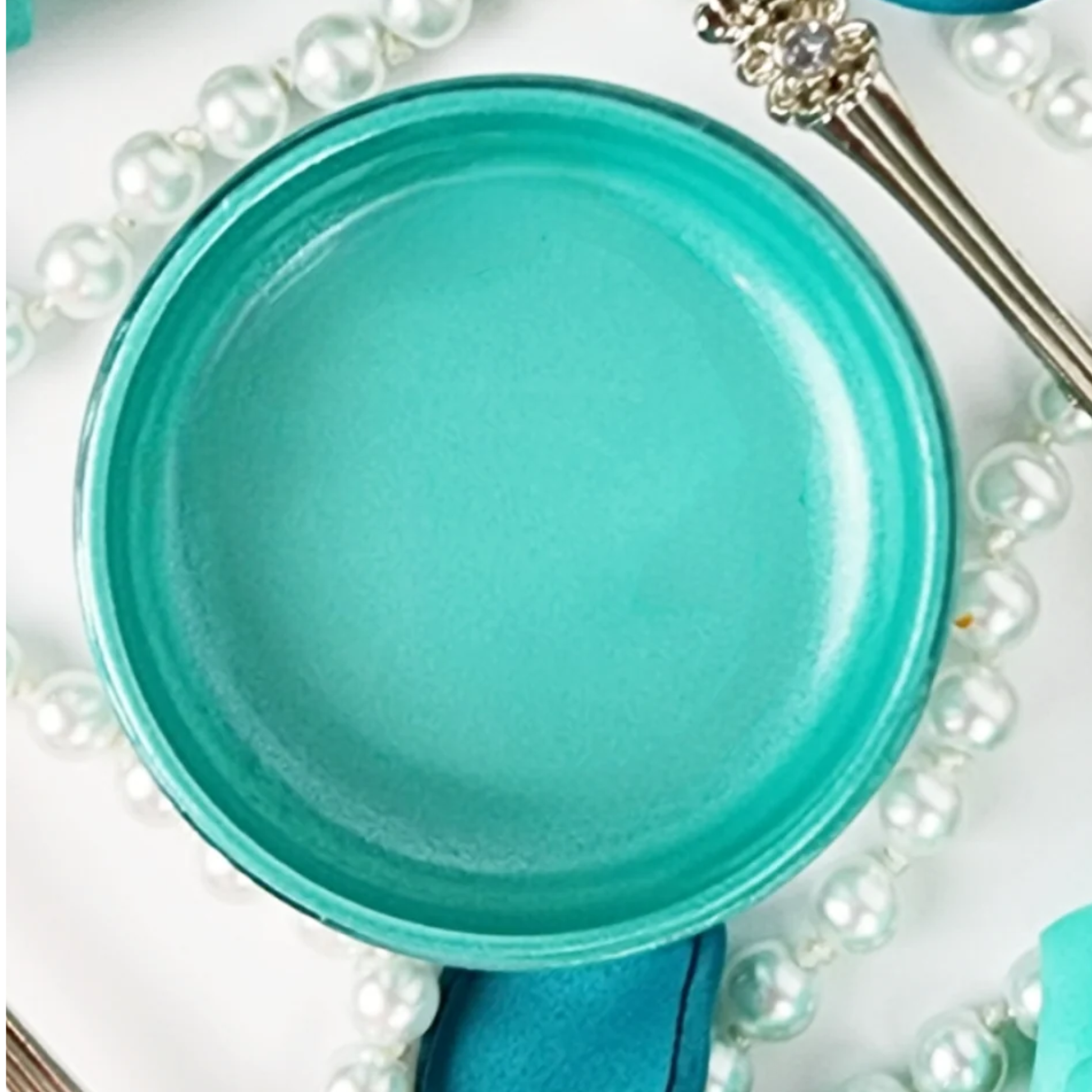 Open jar of turquoise metallic paint with pearls and silverware.