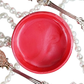 Pot of deep pink metallic paint with a pearl necklace and decorative items on a white background