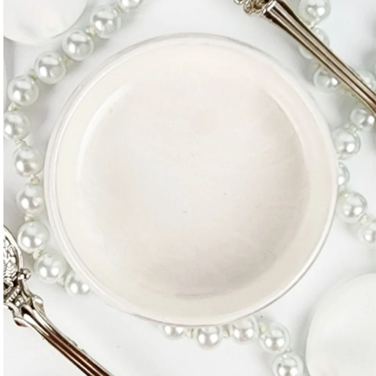 Open jar of off-white metallic paint against a white background with pearls and silverware.