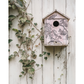 Decorative birdhouse with floral patterns on a white wooden wall with climbing plants.
