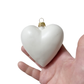 White pufffed heart-shaped ornament held in a hand against a white background
